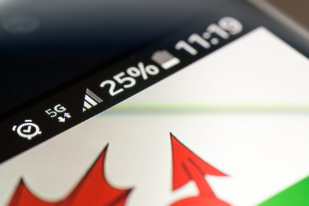 Smartphone on wooden background with 5G network sign 25 per cent charge and Wales flag on the...
