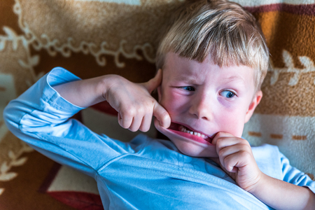 Overhead view little blond boy making silly face on sofaの写真素材
