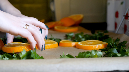Female hands placing orange slices on baking tray tin in kitchenの写真素材