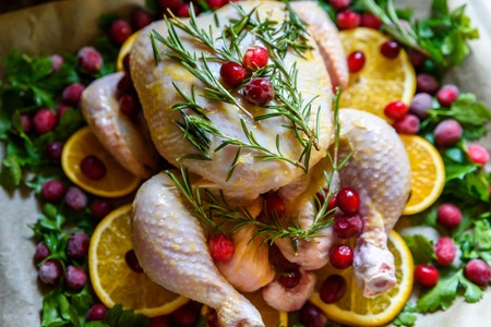 Closeup view of Whole Raw Chicken with Fresh parsley Cranberries and Orange Slices on baking tray tin prepared for roasting in oven.の写真素材