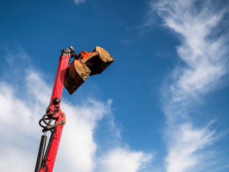 A large red construction excavator bucket over blue sky ready for quarryingの写真素材