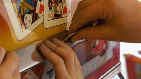 Close-up Of Childs Hands Inserting Coin Into Slots Machineの写真素材