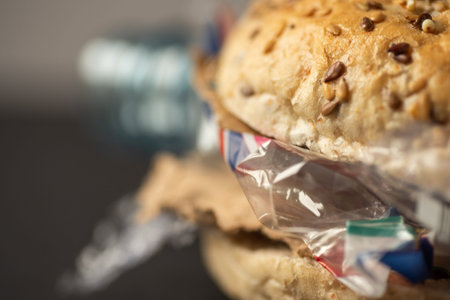 Fresh tasty burger with plastic waste and paper cardboard inside on dark background. Recycled waste...