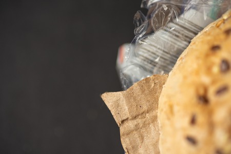 Fresh tasty burger with plastic waste and paper cardboard inside on dark background. Recycled waste in our food conceptの写真素材