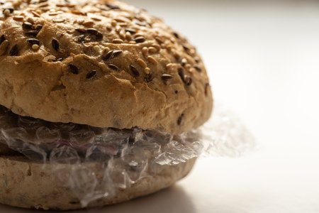 Fresh tasty burger with plastic waste and paper cardboard inside on white background. Recycled waste in our food conceptの写真素材