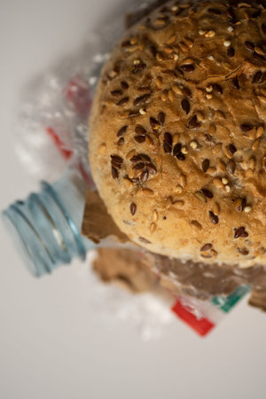 Fresh tasty burger with plastic waste and paper cardboard inside on white background. Recycled waste...