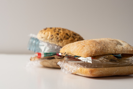 Fresh tasty burger with plastic waste and paper cardboard inside on white background. Recycled waste in our food conceptの写真素材