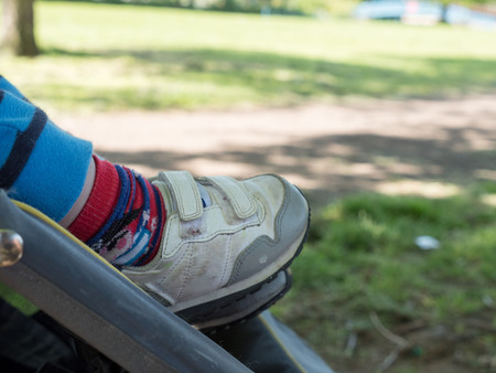 Closeup baby legs in trainers in stroller buggy on a walk in summer parkの写真素材