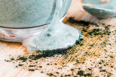 Closeup view fresh kefir probiotik drink in clear glass mixed with green spirulina powder on kitchen...