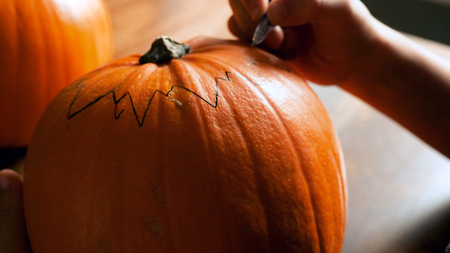 Young boy carving and painting a pumpkin for Halloween on a table.の写真素材
