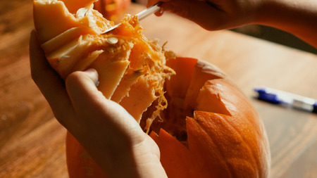 Young boy carving and painting a pumpkin for Halloween on a table.の写真素材