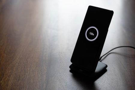 smartphone wireless charging on charging stand with 100 percent icon on screen on wooden table.