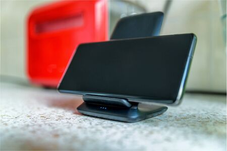 smartphone wireless charging on charging stand on kitchen tabletop.の写真素材