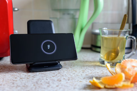 smartphone wireless charging on charging stand with 96 percent icon on screen on kitchen tabletop...