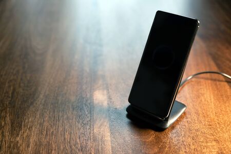 smartphone wireless charging on charging stand on wooden tableの写真素材