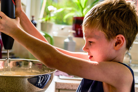 child boy making pancake mix with blender in kitchen