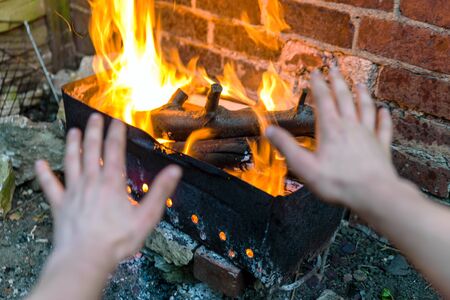 kids warming their arms over fire and grill on red brick wall background in backyard.の写真素材