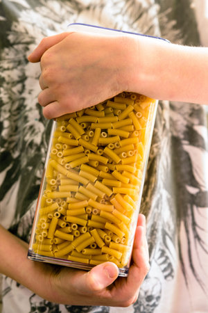 raw italian macaroni pasta inside clear storage container inside childs handsの写真素材