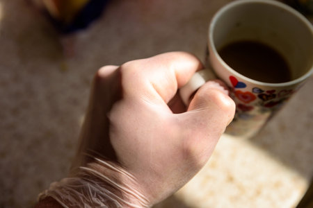 male hand in rubber gloves holding cup tea or coffee during covid 19 lockdownの写真素材