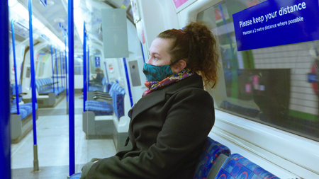 female passenger wearing face covering mask during covid-19 lockdown inside metro train in england...
