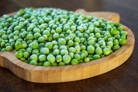 frozen frosty green peas on wooden plate closeupの写真素材
