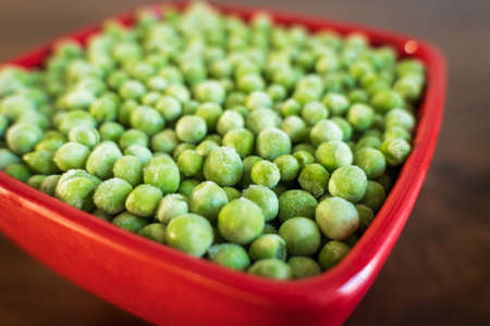 frozen frosty green peas in red ceramic bowl closeupの写真素材