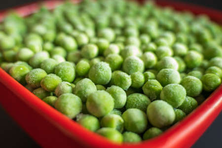 frozen frosty green peas in red ceramic bowl closeupの写真素材