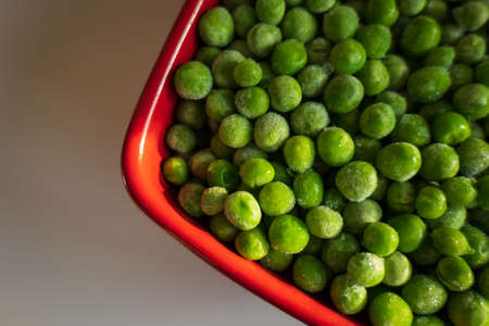 frozen frosty green peas in red ceramic bowl closeupの写真素材