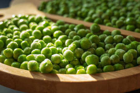 frozen frosty green peas on wooden plate closeupの写真素材