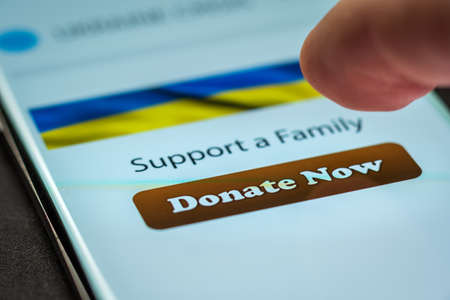 Close-up finger pressing donate button on smartphone screen. Donation money online conceptの写真素材