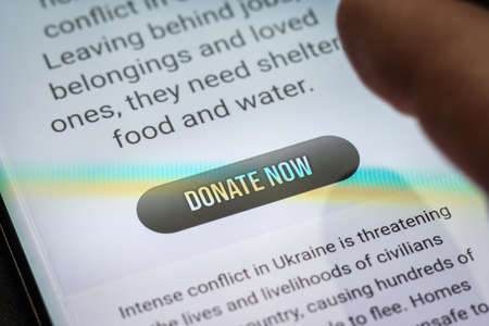 Close-up finger pressing donate icon button on smartphone screen. Donation money online conceptの写真素材
