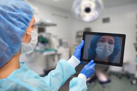 Female doctor in protective suit: medical mask, hat and robe. The woman uses a digital tablet and displays disease statistics on the screen.の写真素材