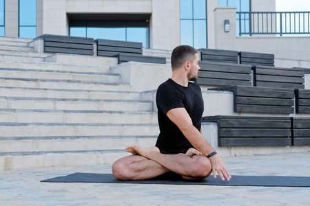 Man athlete in black sportswear practices yoga exercises, stretches, fitness, lotus position,...