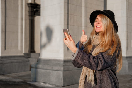 A young woman talks on her smartphone and takes a selfie. A teenager in a gray coat on the street....