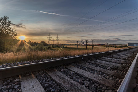 Railroad tracks in the countryside at sunset with sun setting behind the clouds
