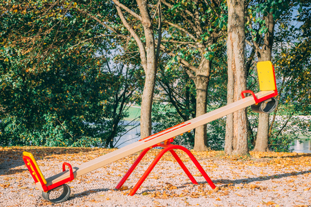 Children playground consisting of carousel, swing. Fallen autumn leaves of trees on the backgroundの写真素材