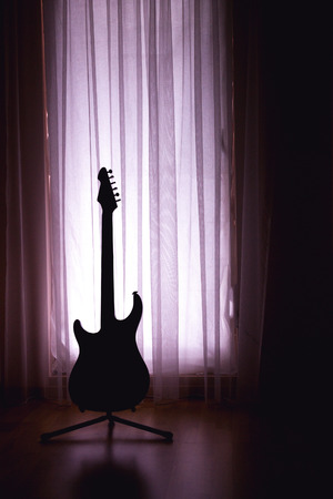 Silhouette of an electric guitar on a purple light background of curtains and a large windowの写真素材