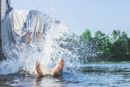 The legs and arms of a person sticking out of a huge amount of water splashing drops in the summer on the lake. Fun water entertainment.の写真素材