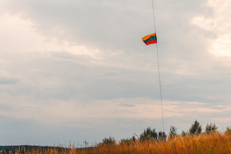 a man holding a Lithuanian flag on a cable aimed at the sky in the summer in a field.の写真素材