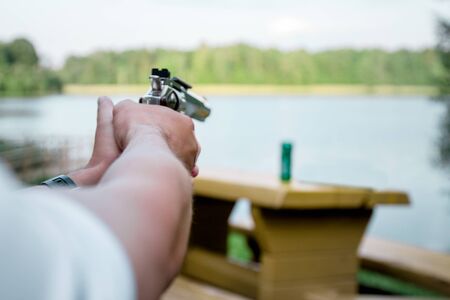 hand of a man aiming a pistol from a revolver into a green bottleの写真素材