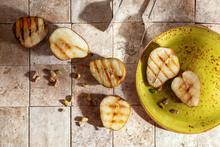 Tasty grilled green pears with pistachio nuts served with honey on green craft plate and earth toned...