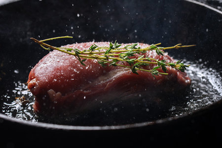 Raw fresh beef steak with seasonings, garlic and rosemary on cast iron frying pan