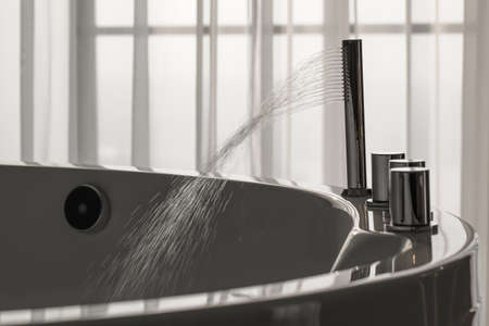 Spout running water from wide bath tube faucet into a hot tubの写真素材