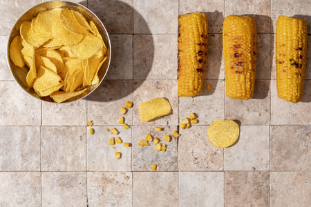 Delicious organic homemade grilled corn cobs and bowl of nacho chips on earth toned stone tales...