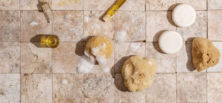 Zero waste bathroom accessories - dry shampoo, natural sea sponge with organic soap foam, skin oil on earth toned stone tales top view direct sunlightの写真素材