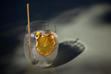 Summer refreshment aperitif cocktail in glass with ice rocks, bamboo straw and eatable flowers on a...
