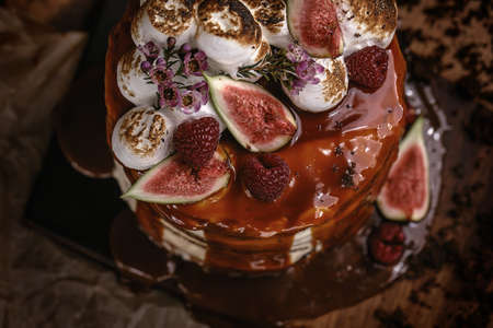 Caramel cake with wild berries, cream and figs on brown backgroundの写真素材