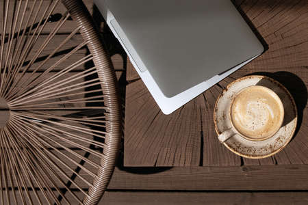 Cup of black coffee with milk in beige craft cup on a solid wood oak coffee table with silver laptop. Cozy space for work at home during lock-down periodの写真素材