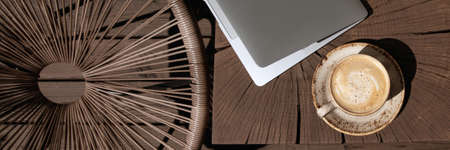 Cup of black coffee with milk in beige craft cup on a solid wood oak coffee table with silver laptop. Cozy space for work at home during COVID-19 lock-down periodの写真素材