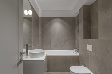 Modern minimalist bathroom beige interior design with marble tiles and beige furniture.
